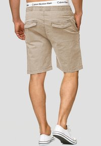 Shorts en coton beige avec une coupe décontractée, dotés de deux poches arrière et d'une ceinture élastique blanche avec le logo "Calvin Klein".
