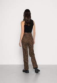 Pantaloni a righe zebrate marroni con vita alta, abbinati a un top senza maniche nero e stivali neri con suola spessa, visti da dietro.