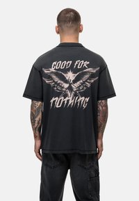 Zwarte T-shirt met korte mouwen, voorzien van een groot ontwerp op de achterkant met een feniks en de tekst "GOOD FOR NOTHING" in vet, verweerd lettertype.