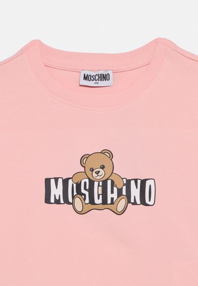 Ροζ βαμβακερό μπλουζάκι με γραφικό ενός καρτούν αρκούδου σε καφέ χρώμα και μαύρο κείμενο που λέει "MOSCHINO" κάτω από την αρκούδα. Στρογγυλή λαιμόκοψη.