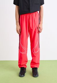Røde atletiske bukser med en løs pasform, elastisk talje, sorte accentstriber langs siderne og hvid syning langs et buet design.