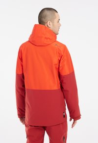 Herrenjacke mit zwei Farbtönen, die einen orangefarbenen oberen Abschnitt und einen dunkelroten unteren Abschnitt aufweist. Hergestellt aus leichtem, wetterfestem Stoff mit Kapuze.