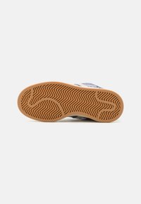 Sneaker sole with a textured brown rubber bottom featuring zigzag patterns, designed for traction, with a white upper portion visible at edge.