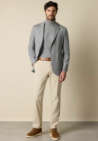 Blazer grigio chiaro sopra un dolcevita grigio, pantaloni beige e scarpe da ginnastica in suede marroni. Presenta un tessuto morbido e una vestibilità su misura.
