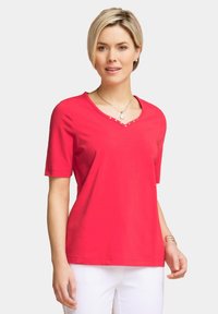 Maglietta in cotone rossa con scollatura a V e maniche corte, caratterizzata da borchie decorative argentate lungo il collo. Tessuto testurizzato, vestibilità casual.