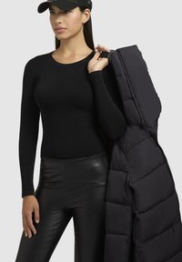 Zwart langmouwtop gecombineerd met glanzende zwarte leren broek. Een puffy zwarte buitenjas is over één schouder gedrapeerd.
