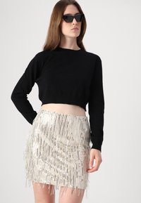 Črn skrajšan pulover v kombinaciji z srebrno mini krilom z resicami, ki vsebuje sijoče kovinske niti. Model nosi črne geometrijske sončna očala.