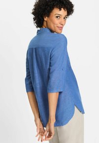 Blue, lightweight, long-sleeve shirt with a collar, button details, and a curved hem. Slightly loose fit with a textured fabric.