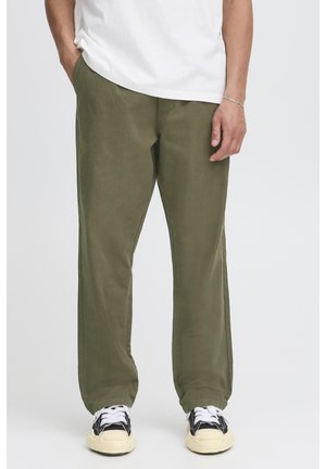 Grüne Baumwollhose mit lockerem Schnitt, geradem Bein und seitlichen Taschen, kombiniert mit schwarzen und weißen Sneakern.