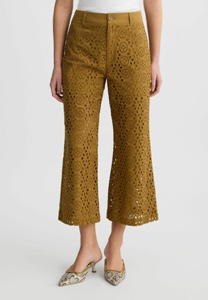 Gehaakte mosterdgele cropped broek met een uitlopende snit en gatenstructuur. Draagt met sleehakken in slangenleerprint.
