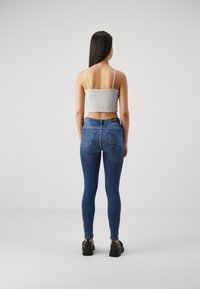 Top corto gris ajustado con dobladillo deshilachado, combinado con jeans ajustados azul oscuro. Modelo lleva zapatos de plataforma negros con detalles de tachuelas.
