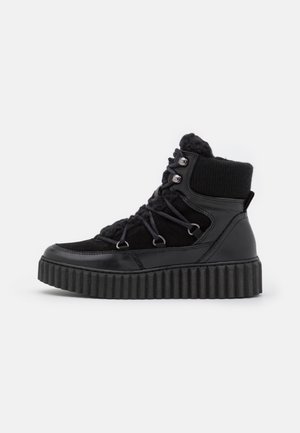 Czarny wysokoprofilowy sneaker z grubą, żebrowaną podeszwą, wyściełanym kołnierzem przy kostce, sznurowaniem z metalowymi oczkami oraz z mieszanki skóry i materiału.