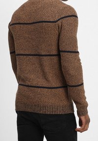 Brun stickad tröja med marinblå horisontella ränder, rundad halsringning och ribbade ärmslut och nederkant, som visar ett texturerat mönster på tyget.