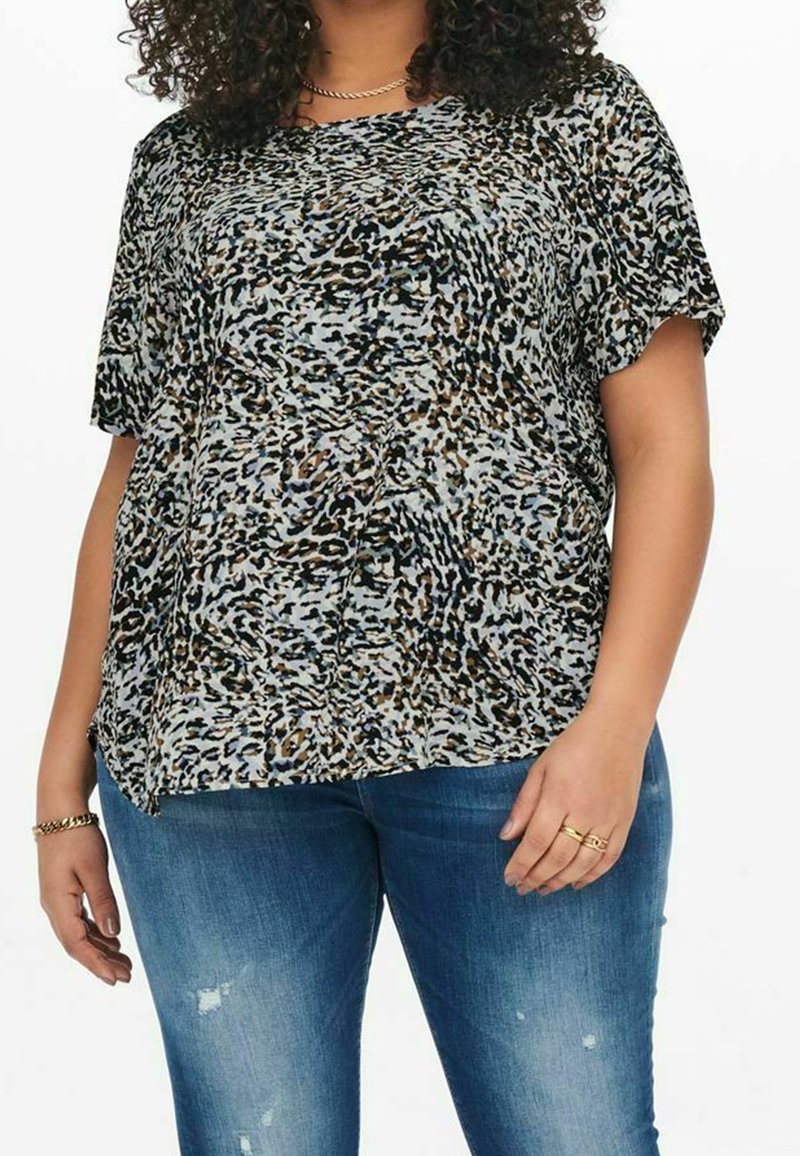 Top con stampa leopardata in azzurro chiaro, maniche corte, vestibilità ampia, texture trasparente, con tonalità di marrone e nero, abbinato a jeans blu scuro.