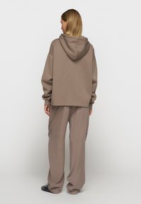 Bruine hoodie met een capuchon, ontspannen pasvorm en lange mouwen, gecombineerd met bijpassende wijde broek. Zachte textuur, minimaal ontwerp en neutrale kleur.