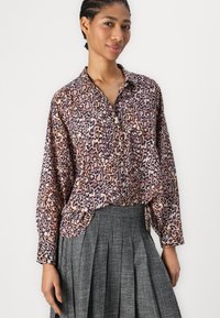 Leopardmønstret bluse i nuancer af pink og brun, med kravehals, knaplukning foran og løs pasform, parret med en mørk plisseret nederdel.