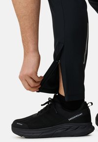 Zwarte sportbroek met ritsopeningen aan de onderbenen, gecombineerd met zwarte waterdichte sneakers met een gestructureerde bovenkant en logodetail.
