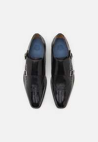 Scarpe in pelle nera con finitura lucida, dettagli brogue, chiusura con fibbia e un motivo testurizzato sulla punta.