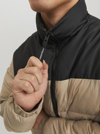 Giubbotto imbottito con parte superiore nera e parte inferiore beige. Presenta un colletto alto, chiusura con zip e maniche arricciate per una maggiore isolamento.