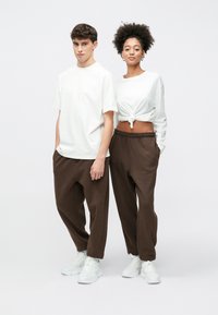 Λευκά μπλουζάκια συνδυασμένα με καφέ, άνετες φόρμες. Στοιχεία που ξεχωρίζουν είναι ο κόμπος στο γυναικείο τοπ και τα λευκά αθλητικά παπούτσια.