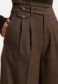 Hnědé kalhoty s houndstooth vzorem, vysokým pasem, dvěma knoflíky v pase a postranními kapsami s viditelnými sklady pro zvýšení textury.