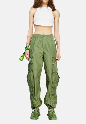 Γυναίκα που φοράει λευκό crop top, πράσινο παντελόνι cargo με πολλές τσέπες, πράσινα αθλητικά παπούτσια και πράσινο μαντήλι με σχέδια στον καρπό.