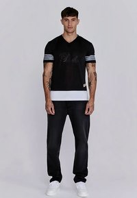 Must v-kaelusega t-särk hõbedaste triipude ja esilogoga varrukatel, kombineeritud tumedate teksade ja valgete tossudega. Omadused: keha järgiv lõige.