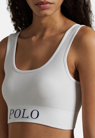 Bílý žebrovaný crop top s širokým tmavě modrým lemem nesoucím slovo "POLO." Hladká textura látky a výstřih do tvaru lodi s širokými ramínky.