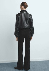 Czarna skórzana kurtka z wysokim kołnierzem, zestawiona z czarnymi rozszerzanymi spodniami. Gładka tekstura z dopasowanym krojem, pokazując widok od tyłu.