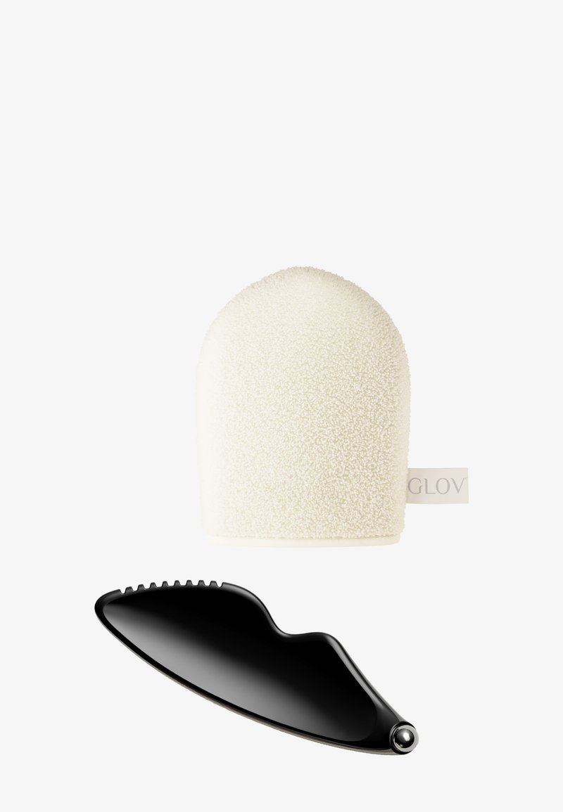 Textured white cleansing glove with rounded top and tag, paired with a sleek black facial massager with curved shape and ridged edge.