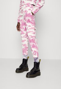 Calças cargo joggers em tie-dye rosa e branco, com múltiplos bolsos e cintura elástica, combinadas com botas de combate pretas com atacadores.