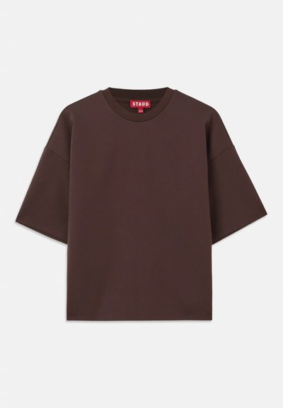 T-shirt oversize marron en coton, avec un col rond, des manches courtes et une étiquette au niveau du col avec un fond rouge.