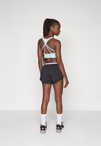 Ljusblå sportbehå med korsad baksidesdesign, kombinerad med svarta shorts. Modellen har på sig svarta och lila sneakers, med vita sportstrumpor.