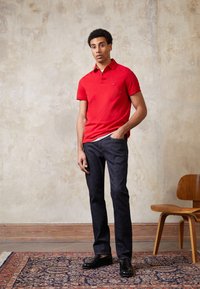 Red polo shirt with short sleeves and a collar, paired with dark denim jeans. Black shoes. Solid colors, casual design, and fitted silhouette.