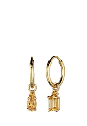 Goldene Creolen mit kleinen hängenden gelben Edelsteinen; ein Ovalschliff und ein Smaragdschliff, auf weißem Hintergrund dargestellt.