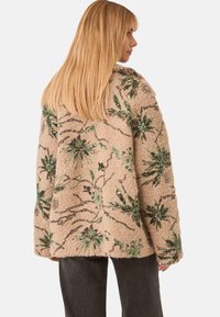 Chaqueta de piel sintética beige con bordado de lentejuelas florales en verde y marrón; corte holgado; mangas largas; textura suave; diseño casual.