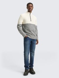 Knit pullover in cream and gray with a half-zip collar, paired with blue jeans and dark boots, showcasing a textured color-block design.