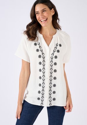 Camicia bianca con bottoni, decorata con ricami neri a fiori e motivi geometrici lungo la parte anteriore; maniche corte; texture stropicciata.