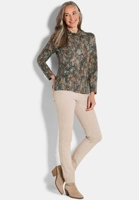 Langsleeve top in een groene, bruine en oranje abstracte patroon; gecombineerd met lichtbeige aansluitende broek en tan enkellaarsjes. Textuurstof.