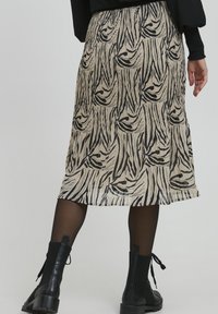 Plisēta svārku kleita ar beidžu krāsu pamatni un melnām zebras raksta svītrām. Tam ir vidēja garuma izmērs un tas lieliski saskan ar melnām potīšu zābakām.