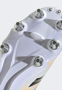 Cleats feature a white plastic sole with six metallic studs, textured surface, and a distinctive geometric design element near the center.
