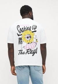 White cotton t-shirt featuring a colorful graphic of a smiling sunflower with sunglasses, surrounded by text, and pink striped details.