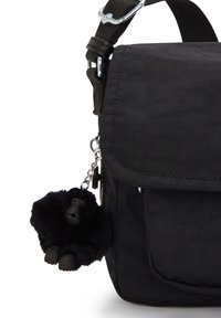 Borsa a spalla in tessuto nero con pattina e tasca frontale, dotata di un piccolo portachiavi gorilla in peluche nero attaccato al lato.
