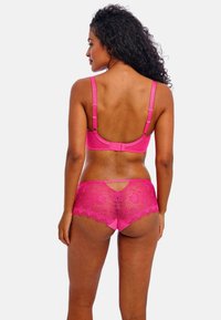 Ensemble de lingerie rose comprenant un soutien-gorge rembourré et lisse ainsi que des culottes en dentelle. Le soutien-gorge possède des bretelles ajustables et une fermeture à crochets ; les culottes présentent des détails en dentelle florale.