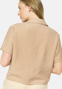 Short-sleeve, collared shirt in light beige, made of textured fabric with a relaxed fit and a slightly cropped hem.