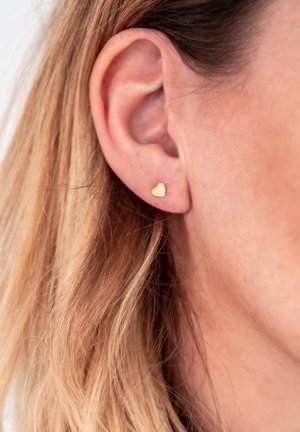 Boucle d'oreille en forme de cœur en or affichée dans l'oreille. Fabriquée en métal avec une texture lisse et un design simple.