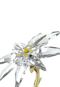Spilla a forma di fiore in cristallo con petali appuntiti, design trasparente e sfaccettato, con abbellimenti gialli al centro e una chiusura in metallo dorato.