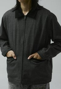 Chaqueta negra con cremallera y cuello de pana, confeccionada en tejido texturizado, con bolsillos tipo deslizantes y un diseño de corte relajado.
