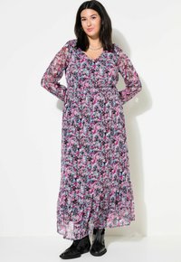 Robe longue à fleurs avec un fond noir, ornée de fleurs roses et bleues, avec des manches transparentes, un décolleté en V et une taille froncée, accompagnée de bottes noires.