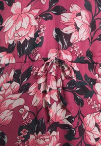Tissu rose avec un grand imprimé floral blanc et noir, présentant un nœud noué à la couture de la taille.